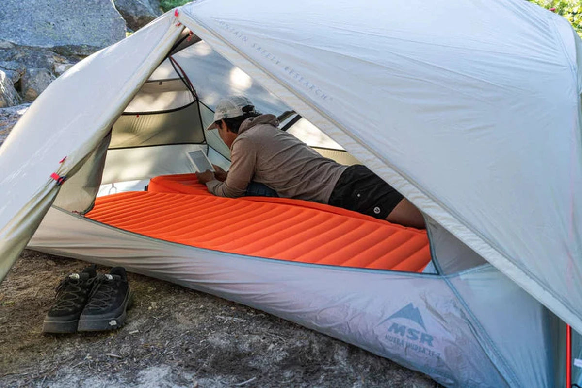 Person använder surfplatta liggande på orange NeoLoft liggunderlag i tält