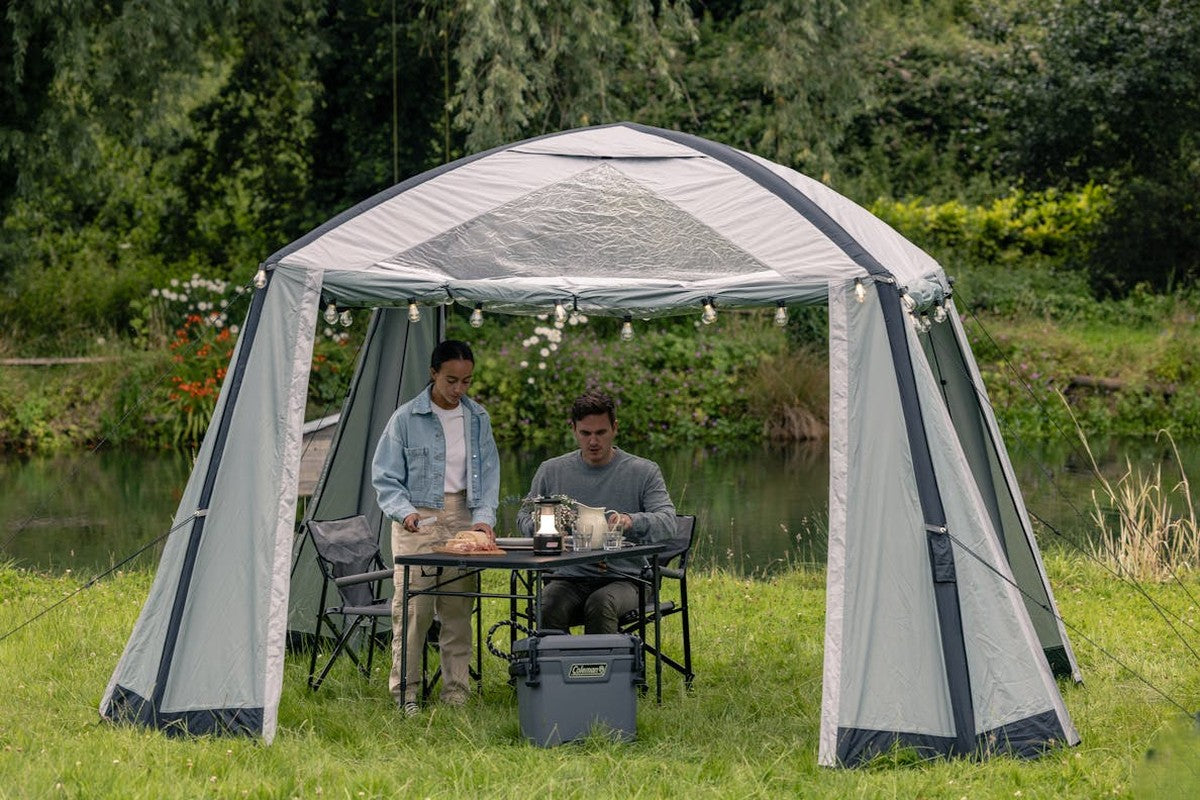 Par som äter middag vid campingbord under tält vid vatten