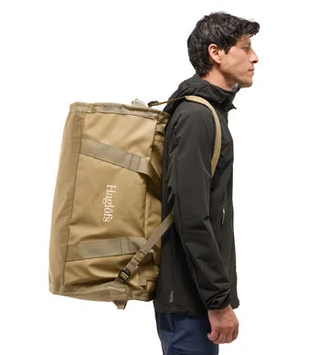Man som bär beige Lava 90 duffelväska som ryggsäck i profil