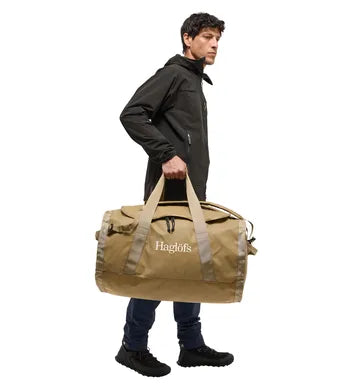Man håller beige Lava 90 väska i sidohandtaget för bärvänlighet