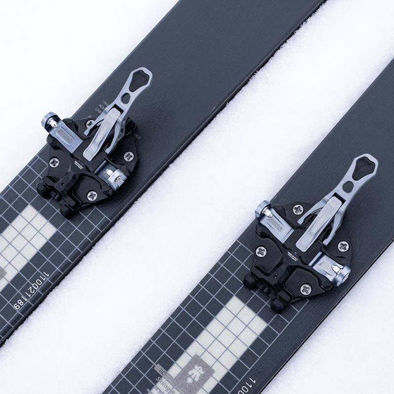 Svarta och silver ATK-bindingar monterade på skidor med rutnätsmönster i snö