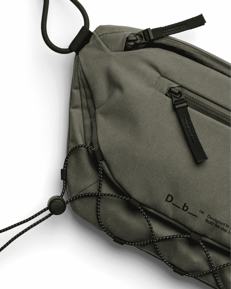 Närbild på mörkgrön slingväska som visar ripstop-textur och dragkedjeficka