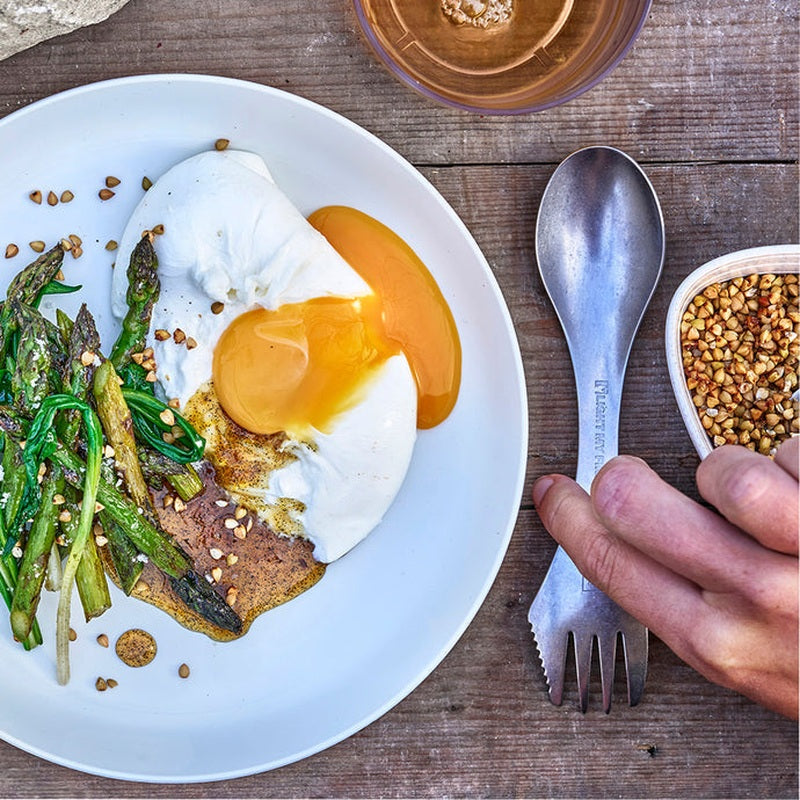 Hand håller spork bredvid tallrik med ägg och asparges