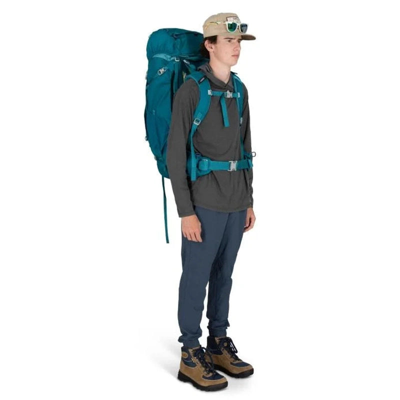 Man i profil som bär teal Osprey Ace 65 ryggsäck utomhus