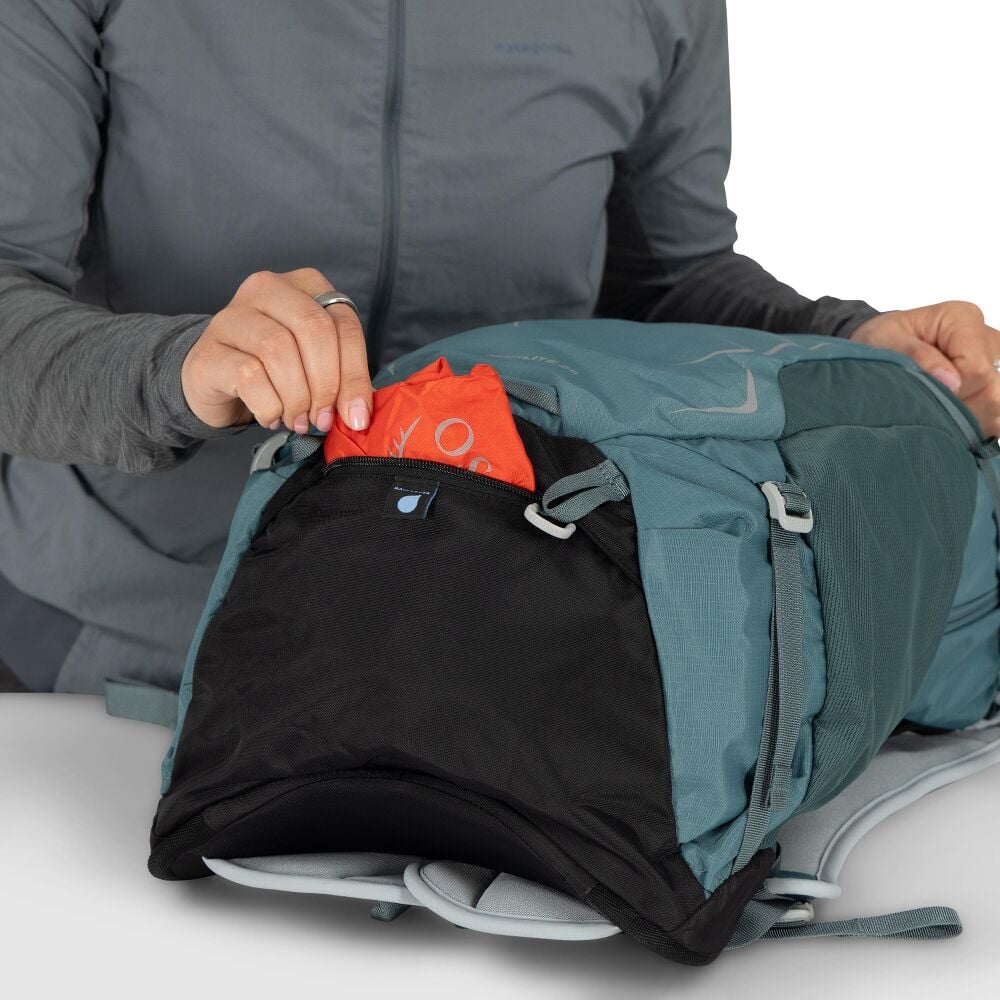 Person öppnar nedre ficka på teal Osprey Hikelite 26 för packning