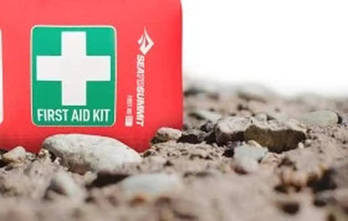 Orange first aid dry bag standing on gravel with green label