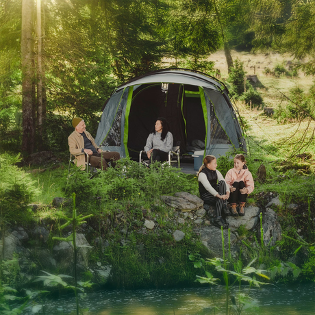 Campingtält och två campingredo personer som står framför tältet med campingprylar