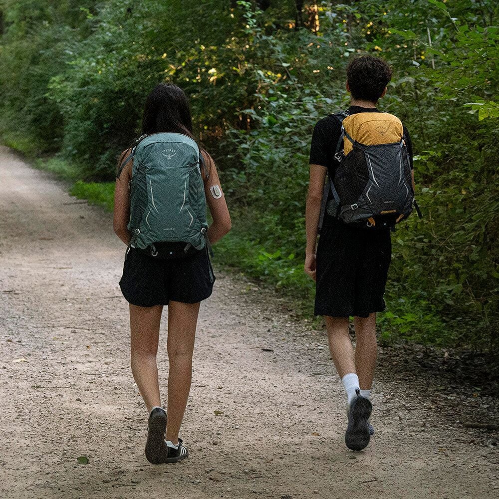 Par som vandrar i skog, kvinna bär teal Osprey ryggsäck