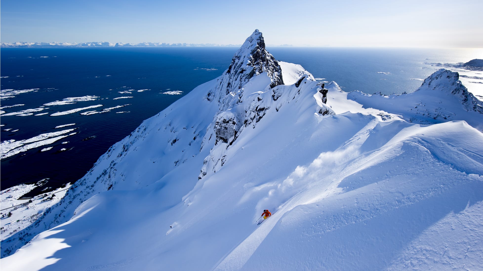 en person som åker ner efter en snötäckt bergssida med utsikt öven en fjord